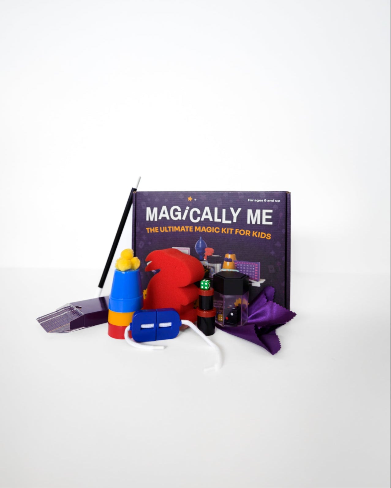 Unboxed contents of Magically Me magic set neatly arranged on white background: custom deck of playing cards, cup & balls, disappearing coin, levitating worm, and more classic magic props for beginners to pros