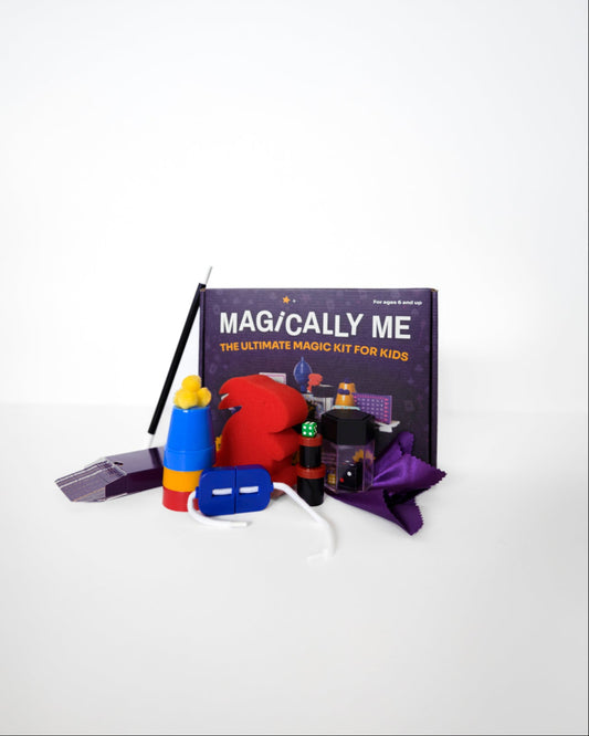 Unboxed contents of Magically Me magic set neatly arranged on white background: custom deck of playing cards, cup & balls, disappearing coin, levitating worm, and more classic magic props for beginners to pros