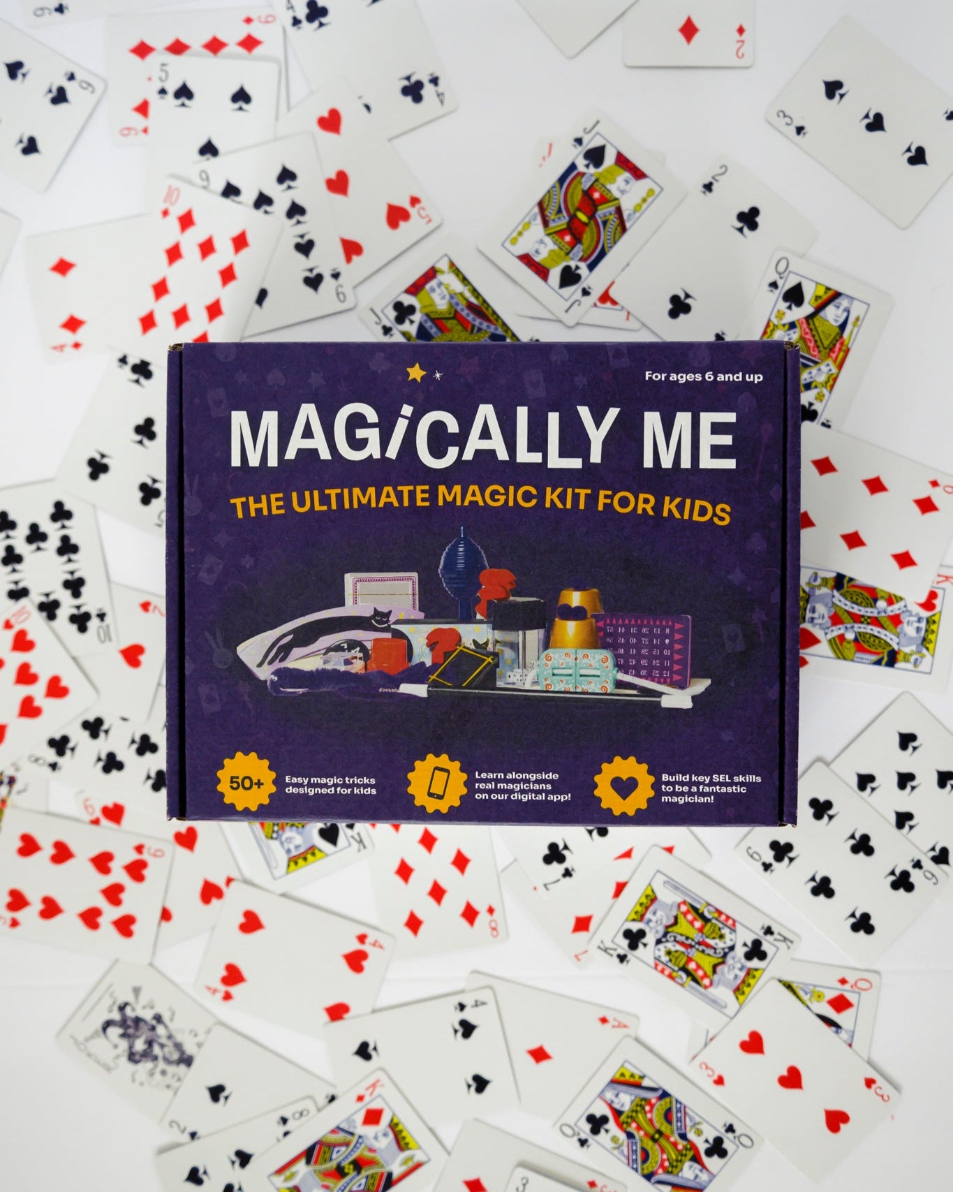 Magically Me Kids Magic Kit box centered on white background, surrounded by a fanned spread of custom playing cards from beginner to pro tricks, inclusive design branding, SEL learning badge, and 1‑Year Premium App Subscription call‑out