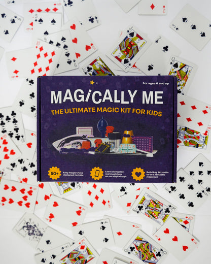 Magically Me Kids Magic Kit box centered on white background, surrounded by a fanned spread of custom playing cards from beginner to pro tricks, inclusive design branding, SEL learning badge, and 1‑Year Premium App Subscription call‑out