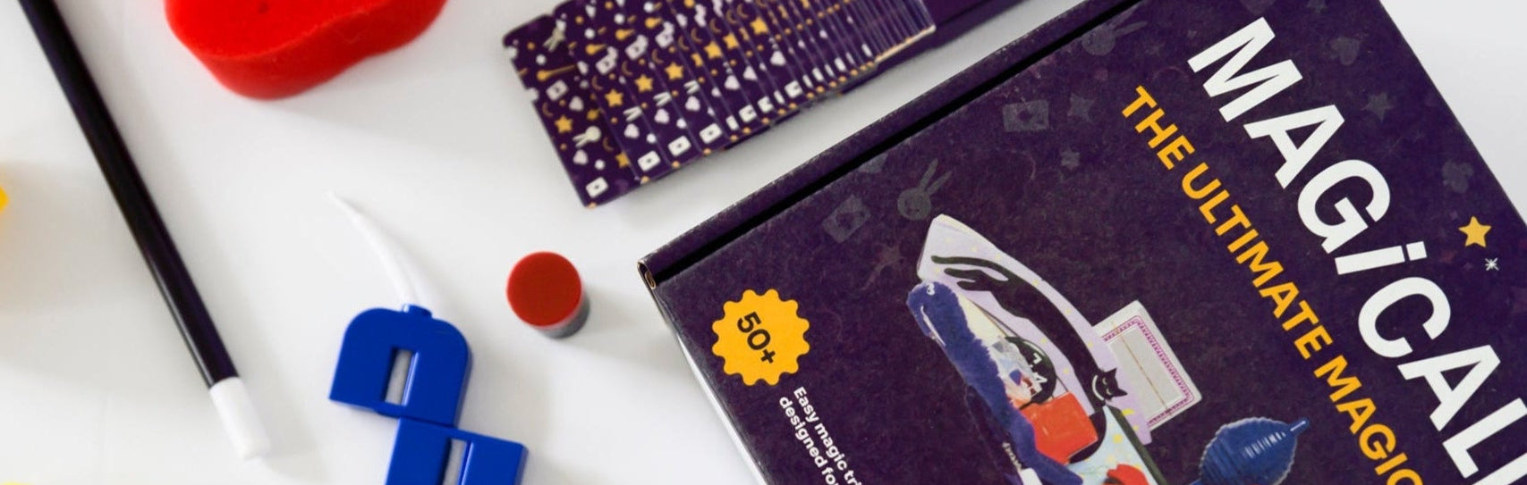 Unboxed contents of Magically Me magic set neatly arranged on white background: custom deck of playing cards, cup & balls, disappearing coin, levitating worm, and more classic magic props for beginners to pros. SEL and inclusive magic kit for children.