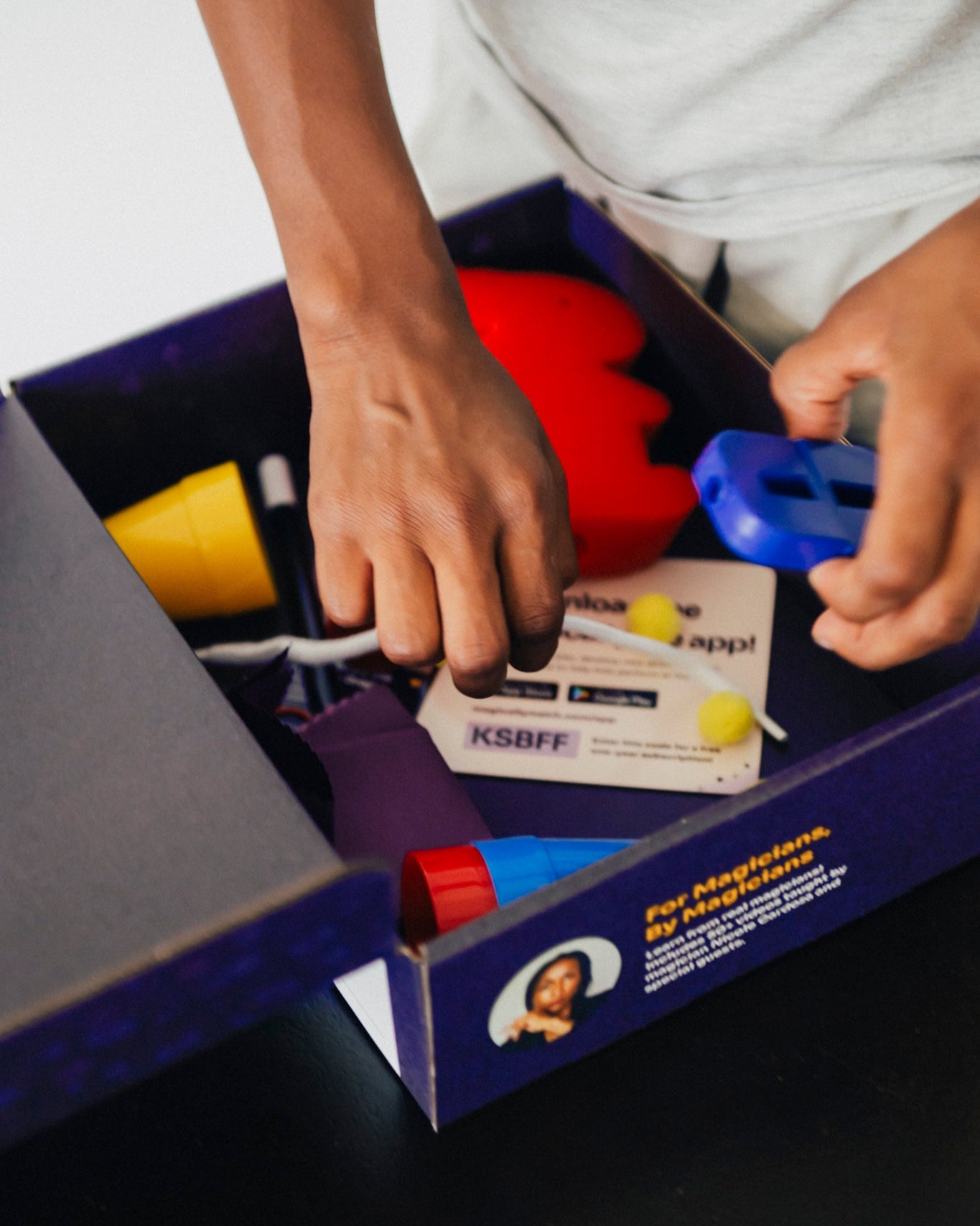 Children’s hands exploring an open Magically Me Kids Magic Kit box, lifting custom playing cards, cup & balls, and disappearing coin—an inclusive beginner‑to‑pro magic set with built‑in SEL learning prompts (ships in 1–2 weeks)